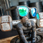 Goodr Silverback Squat Mobility Sunglasses sitting on a barebell; with matte black frames and silver polarized lenses, designed for high-intensity workouts with a no-slip fit, available at Be Charmed