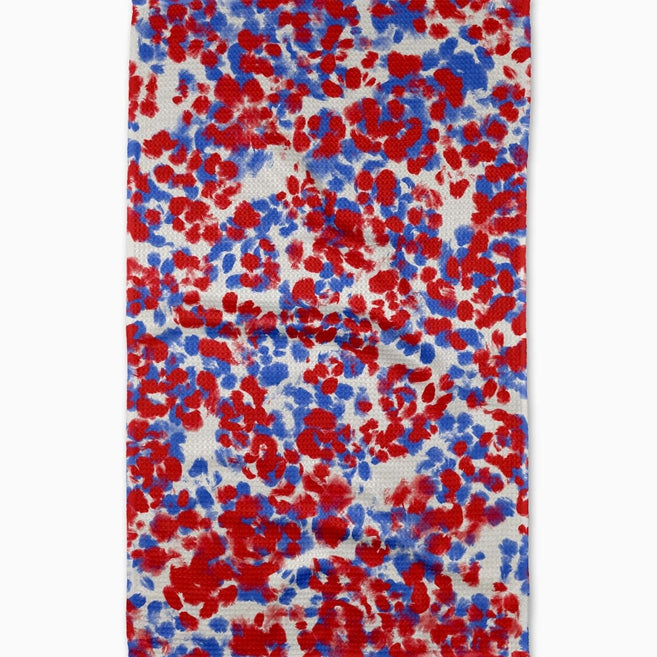 eometry Fire Cracker Tea Towel – White microfiber towel featuring a vibrant pattern of red and blue fireworks, made from recycled materials, available at Be Charmed.