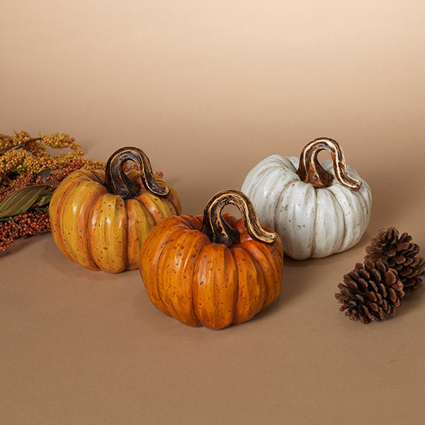 Three decorative pumpkins on a beige surface with a pine cone. Available at Be Charmed