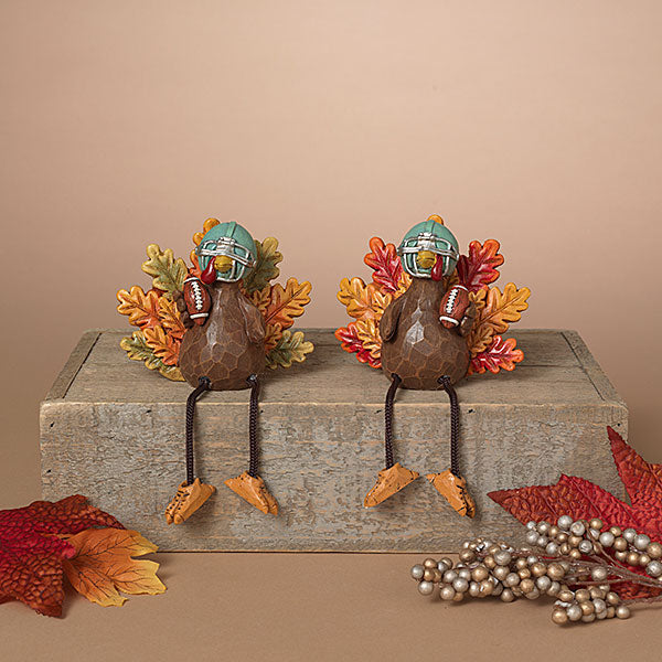 Two decorative turkeys with football helmets and scarves on a wooden block with fall leaves and berries. Available at Be Charmed