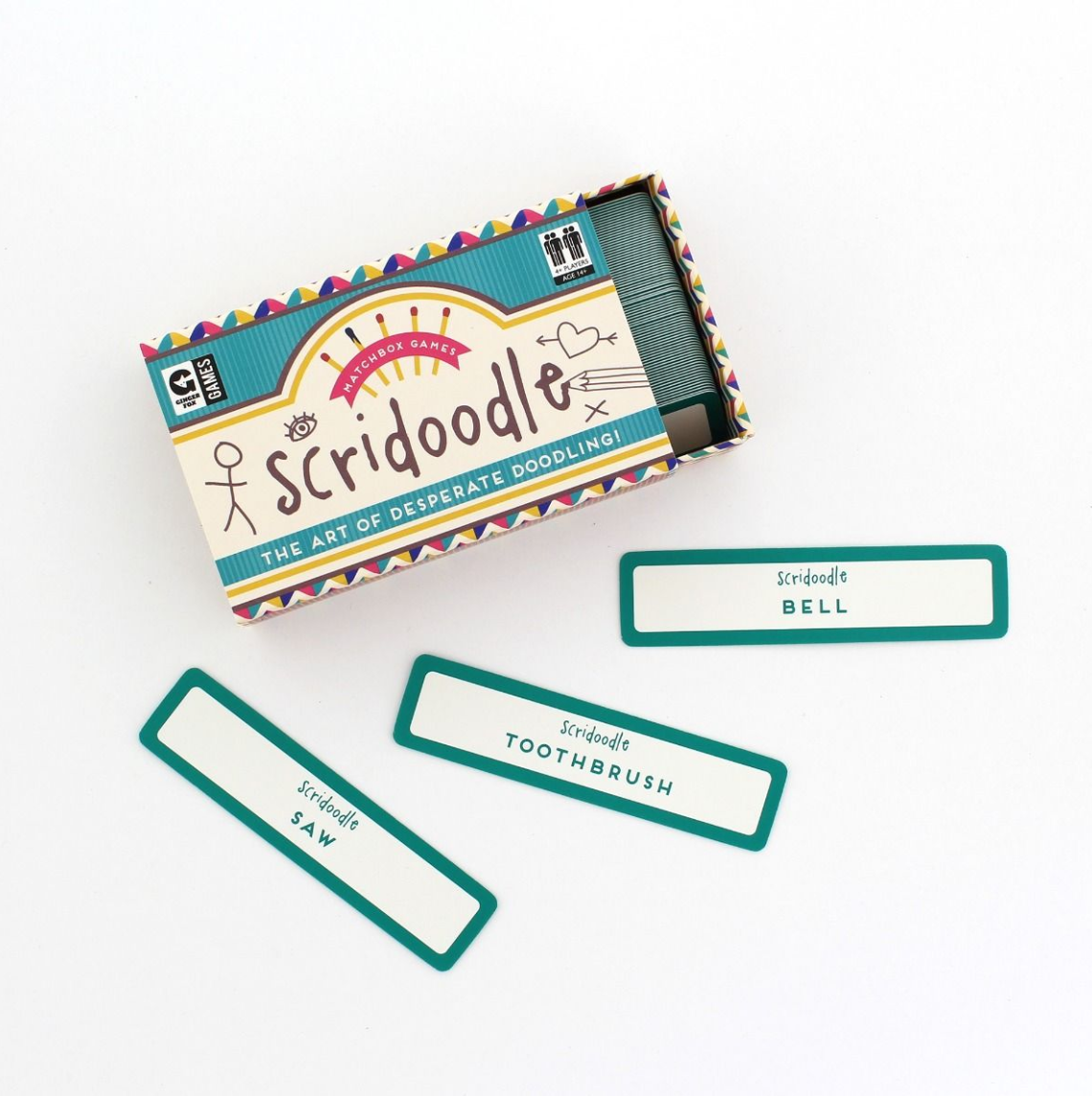A colorful matchbox game set called 'Scridoodle' with various game pieces including cards and a spinner, displayed in front of its packaging box. Available at Be Charmed