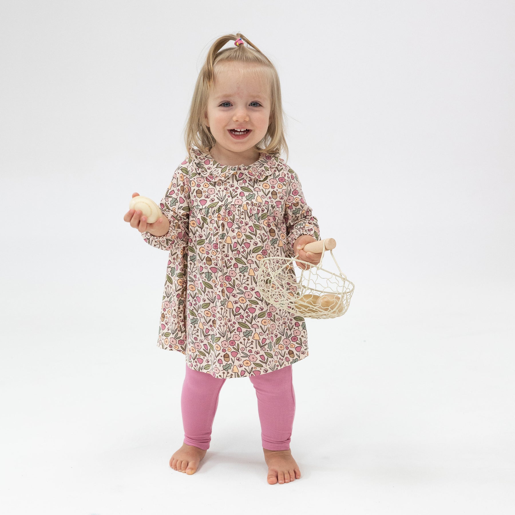 Girl wearing Angel Dear Acorn Floral Ruffle Dress and Leggings set for baby girls, featuring a delicate floral pattern and soft materials, available at Be Charmed.