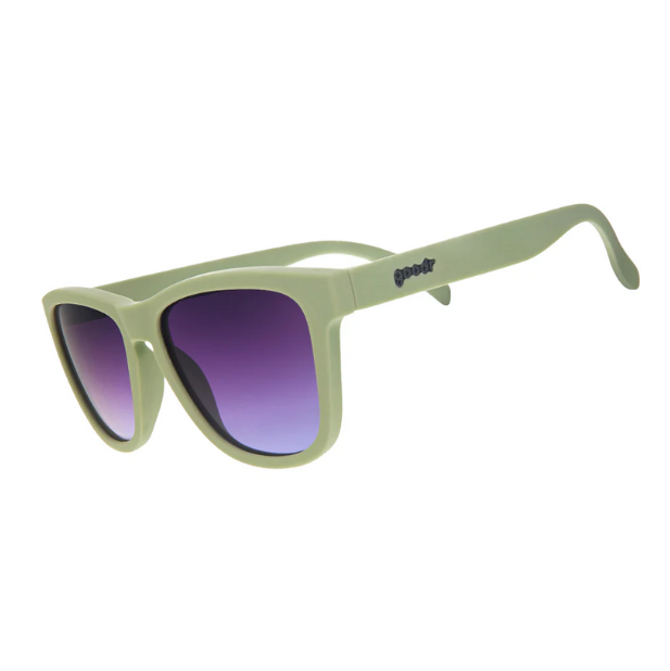 A pair of sage green sunglasses with purple gradient lenses, in a classic OG shape. Available at Be Charmed