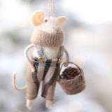 Decorative mouse ornament wearing a sweater and plaid skirt, holding a basket, against a blurred natural background. Available at Be Charmed