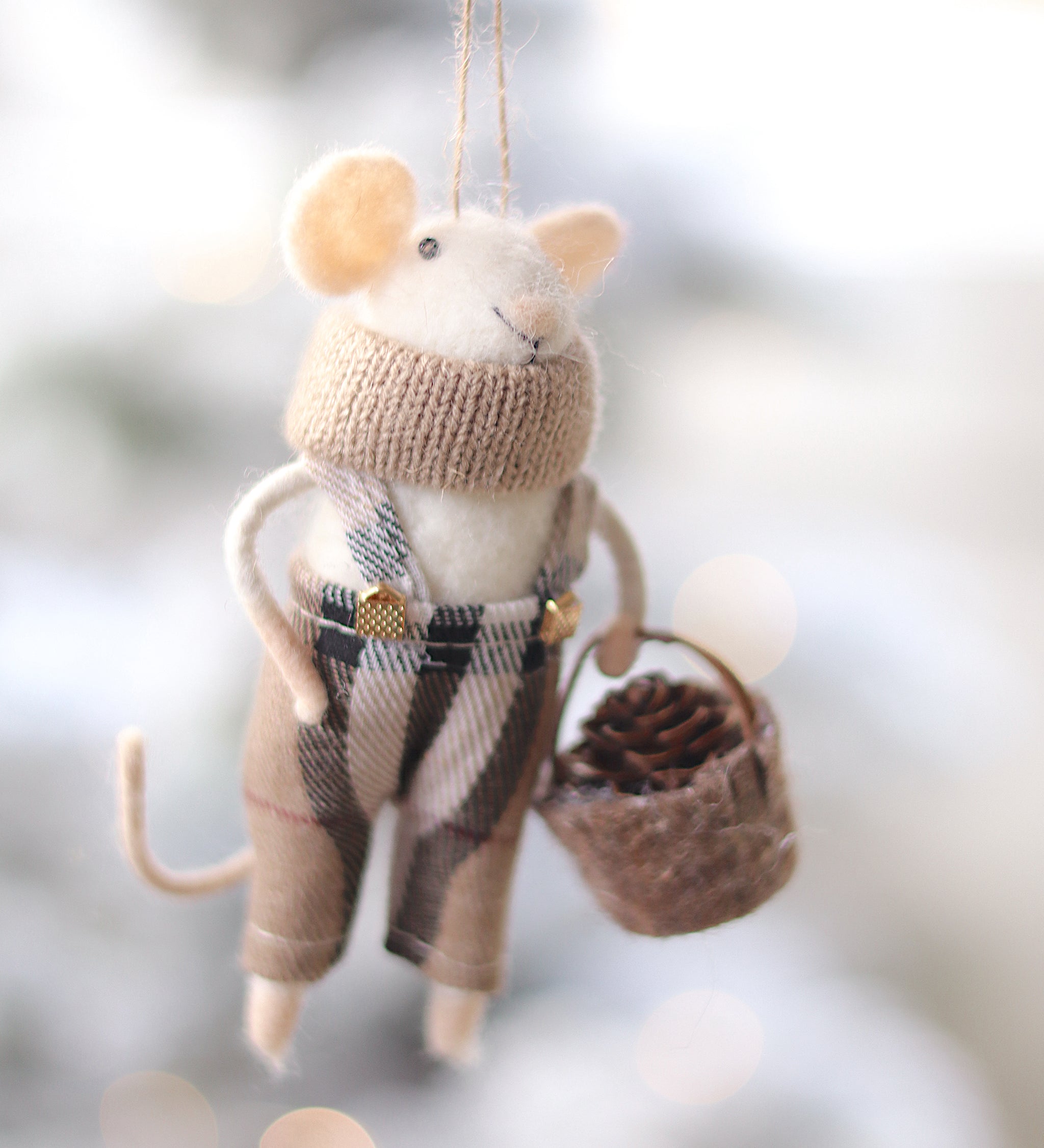 Decorative mouse ornament wearing a sweater and plaid skirt, holding a basket, against a blurred natural background. Available at Be Charmed