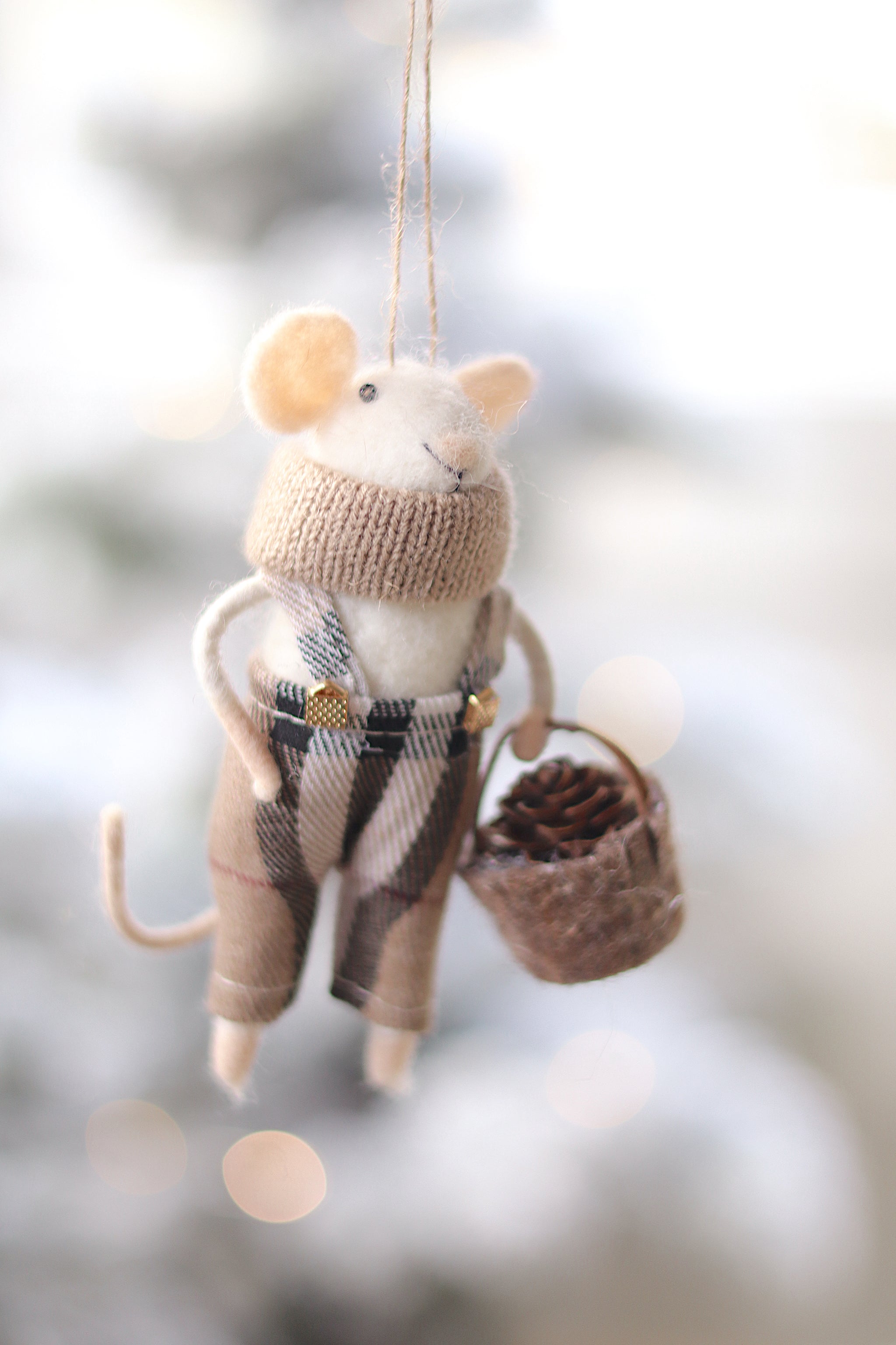 Decorative mouse ornament wearing a sweater and plaid skirt, holding a basket, against a blurred natural background. Available at Be Charmed
