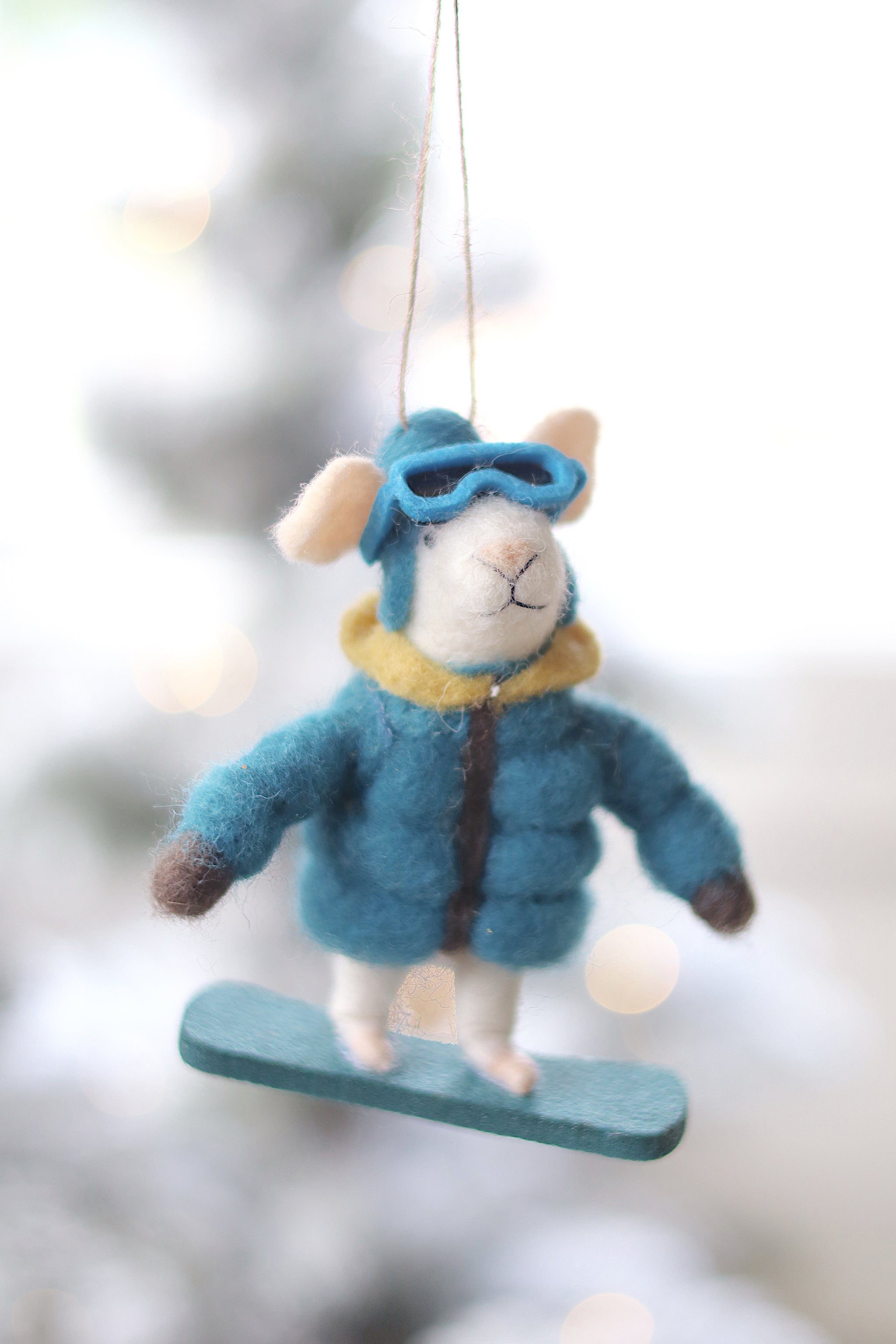 Decorative ornament of a mouse in winter clothing hanging against a blurred snowy background. Available at Be Charmed