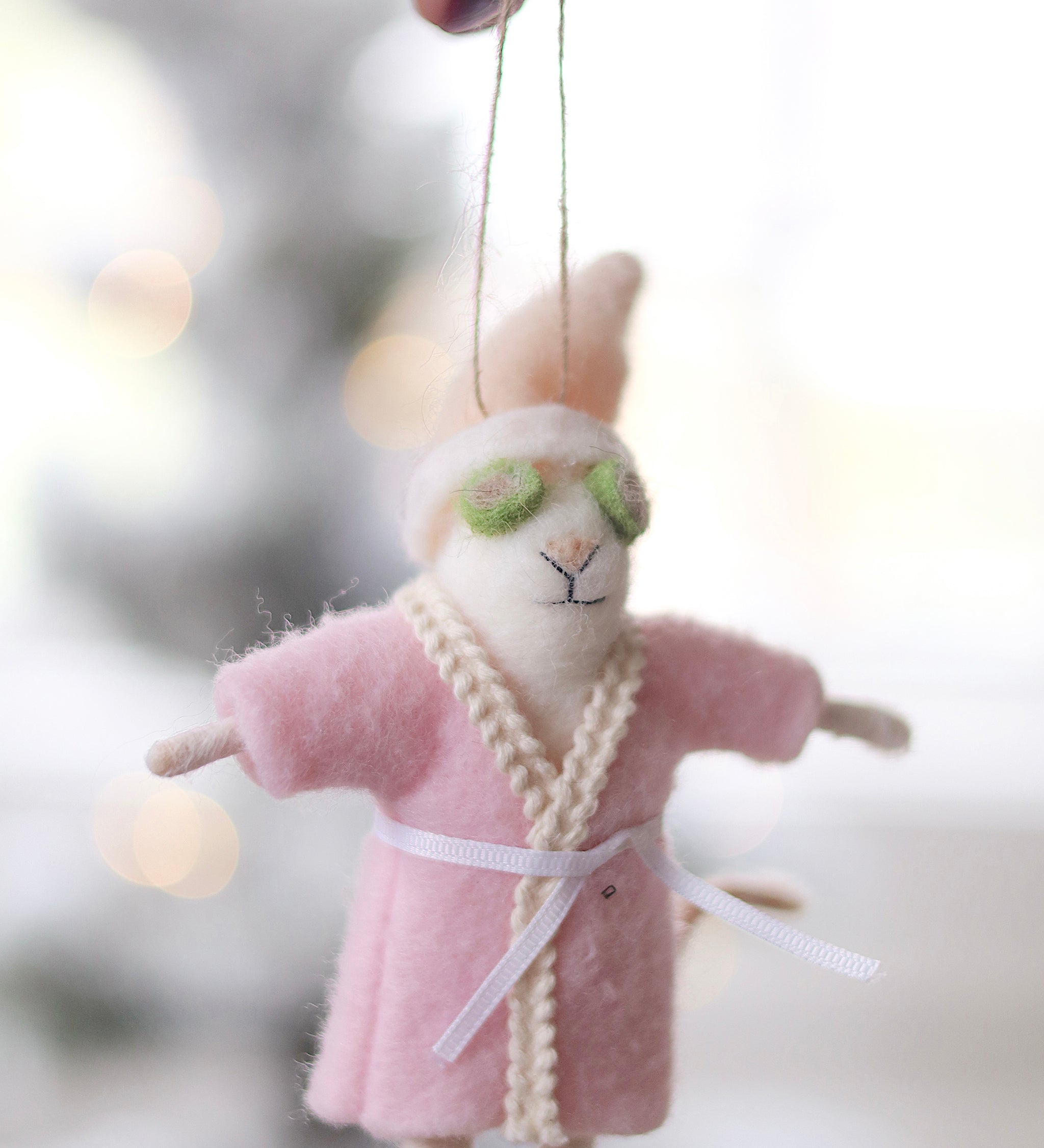 Person holding a plush mouse ornament in a pink robe with green glasses, hanging against a blurred background. Available at Be Charmed
