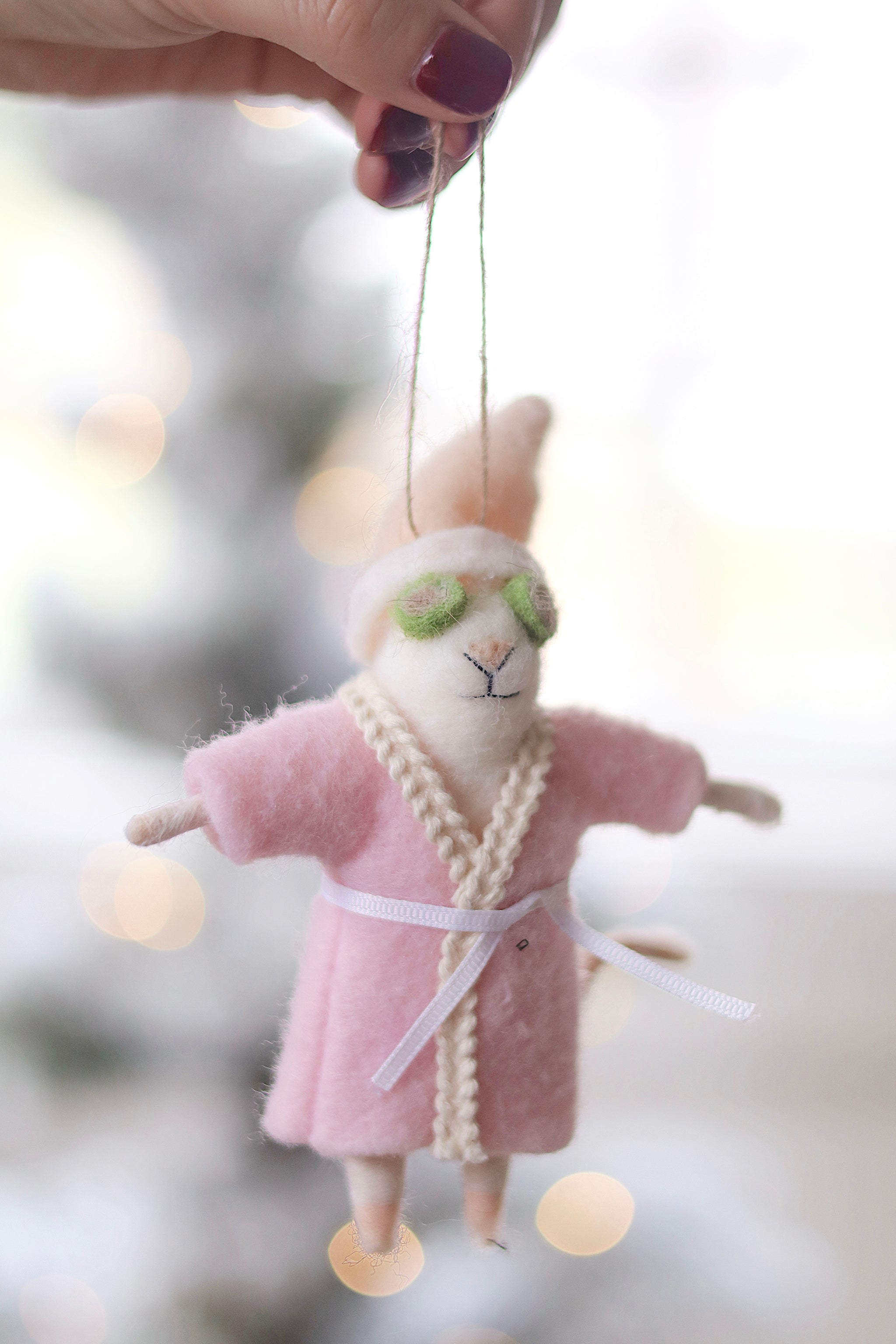 Person holding a plush mouse ornament in a pink robe with green glasses, hanging against a blurred background. Available at Be Charmed
