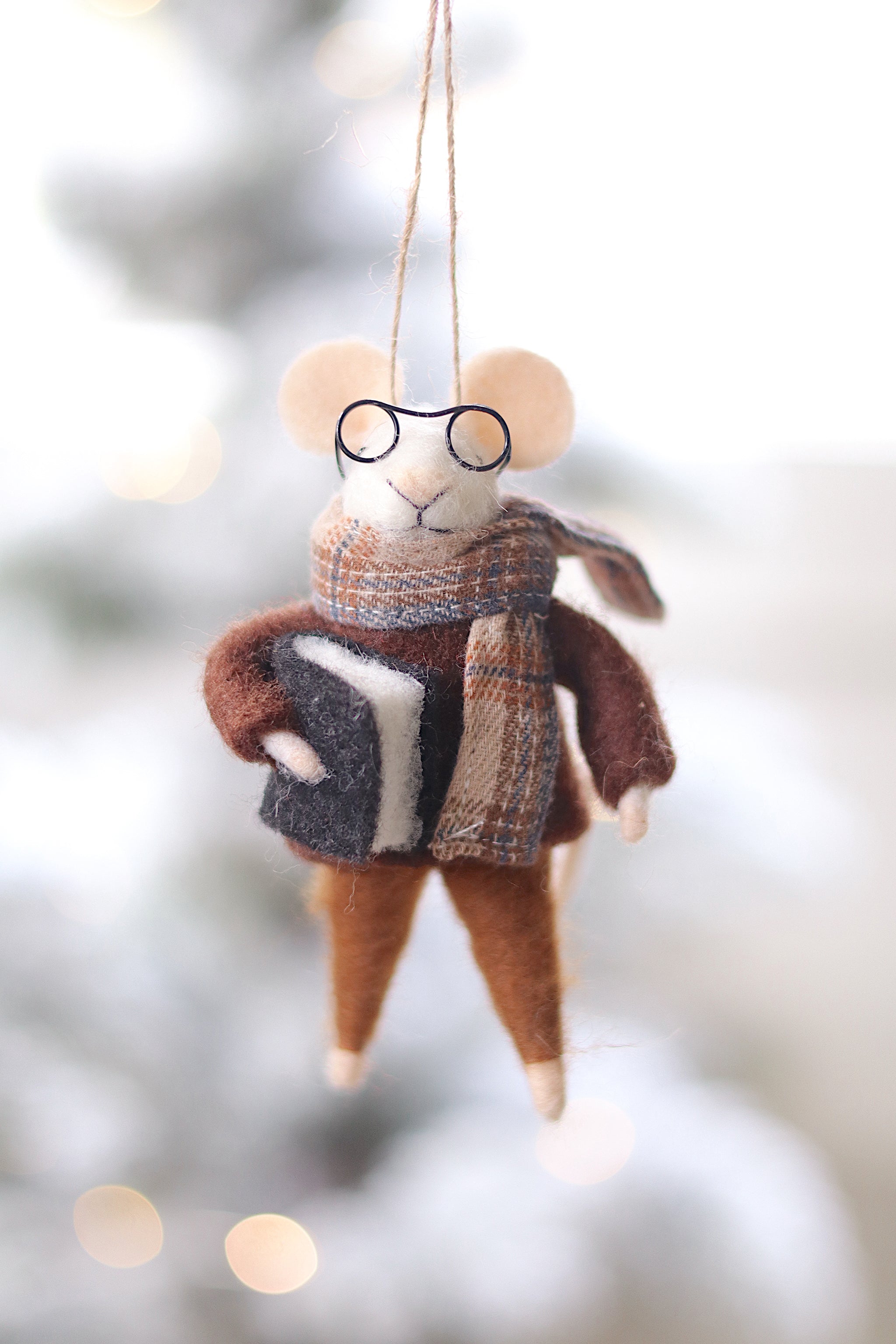 Felt mouse ornament with glasses and a scarf hanging against a blurred natural background. Available at Be Charmed