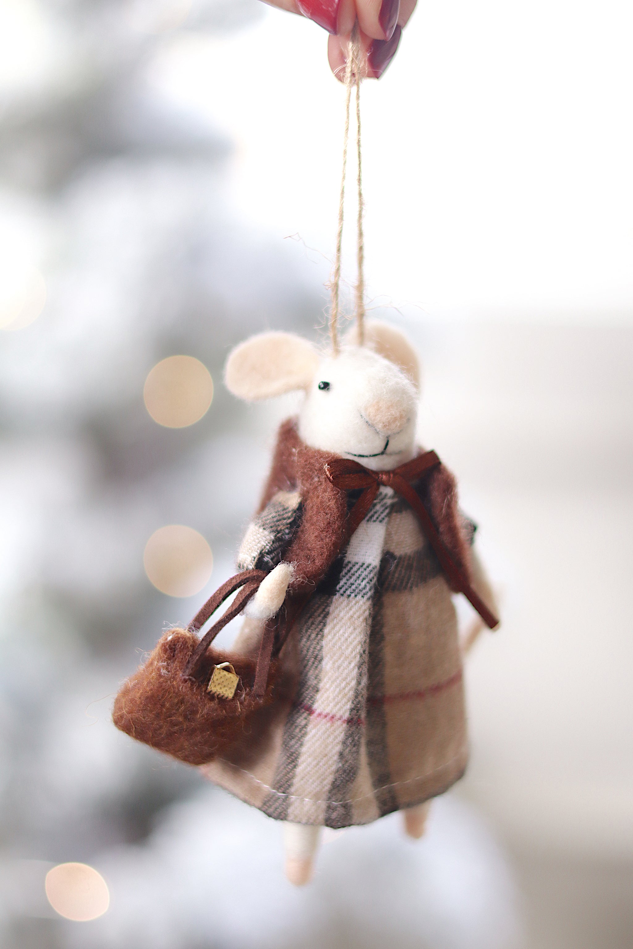 Felted mouse ornament with plaid dress and scarf, held against a blurred snowy background. Available at Be Charmed