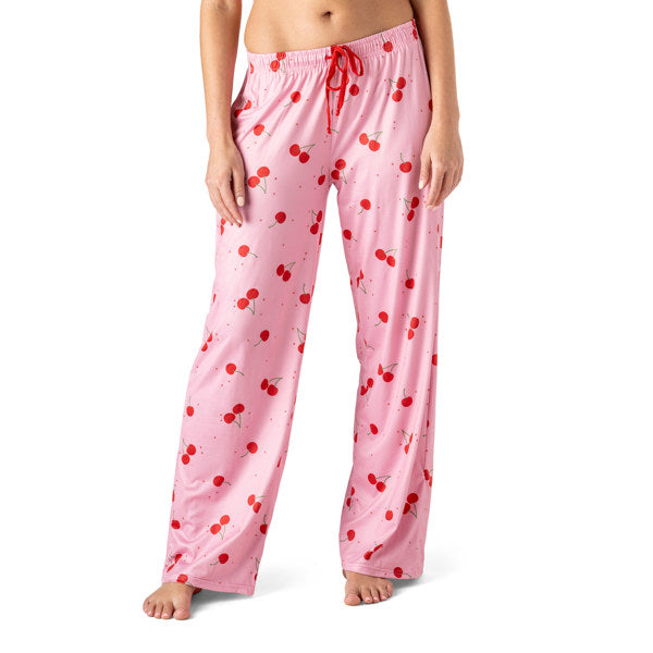 Pink pajama pants with red cherry pattern worn by a person on a white background. Available at Be Charmed