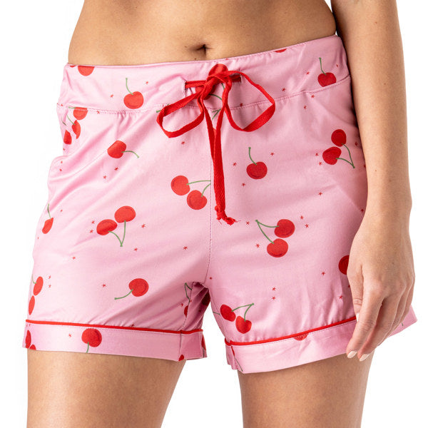 Pink pajama shorts with cherry pattern and red drawstring on a white background. Available at Be Charmed
