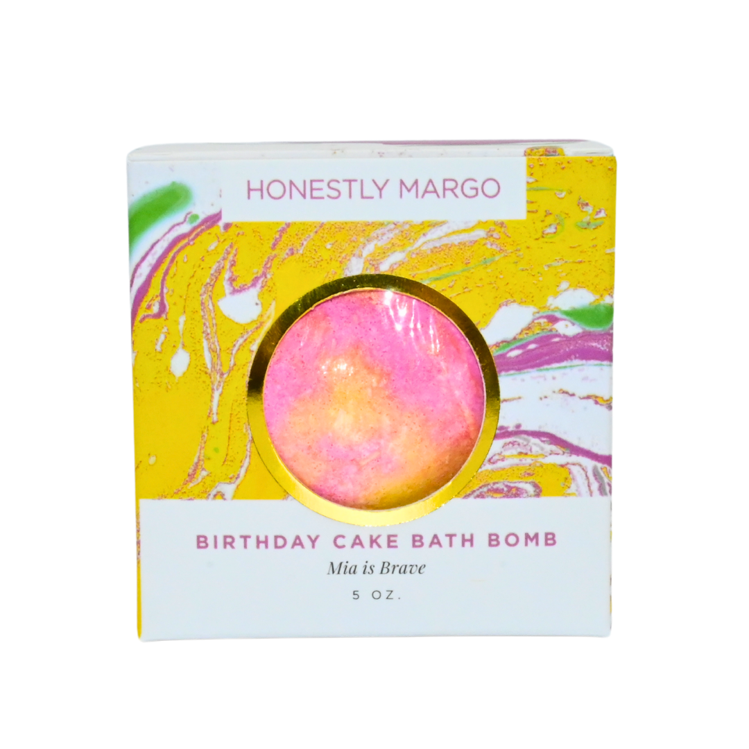 Birthday cake bath bomb packaging with 'Honestly Margo' branding on a white background. Available at Be Charmed