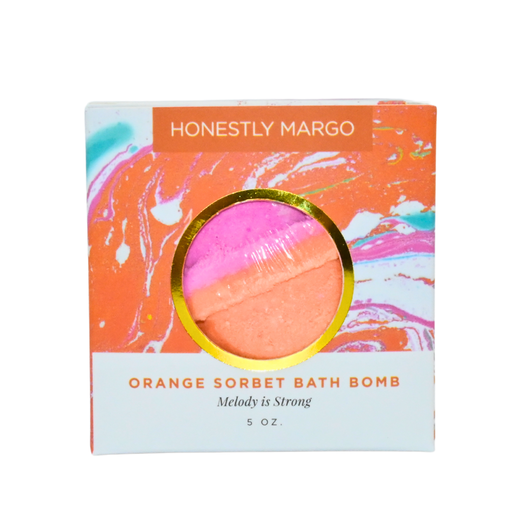 Orange sorbet bath bomb packaging with 'Honestly Marg' branding on a white background. Available at Be Charmed