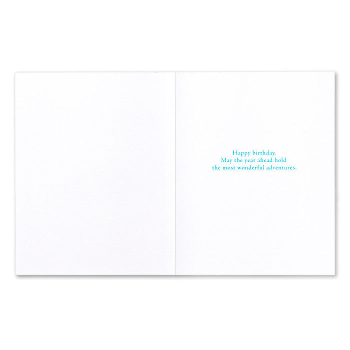 White card with blue text 'Happy birthday, May the year ahead hold the most wonderful adventures.' Available at Be Charmed