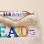 Cream-colored fleece pouch with colorful 'READ' text and striped interior. Available at Be Charmed
