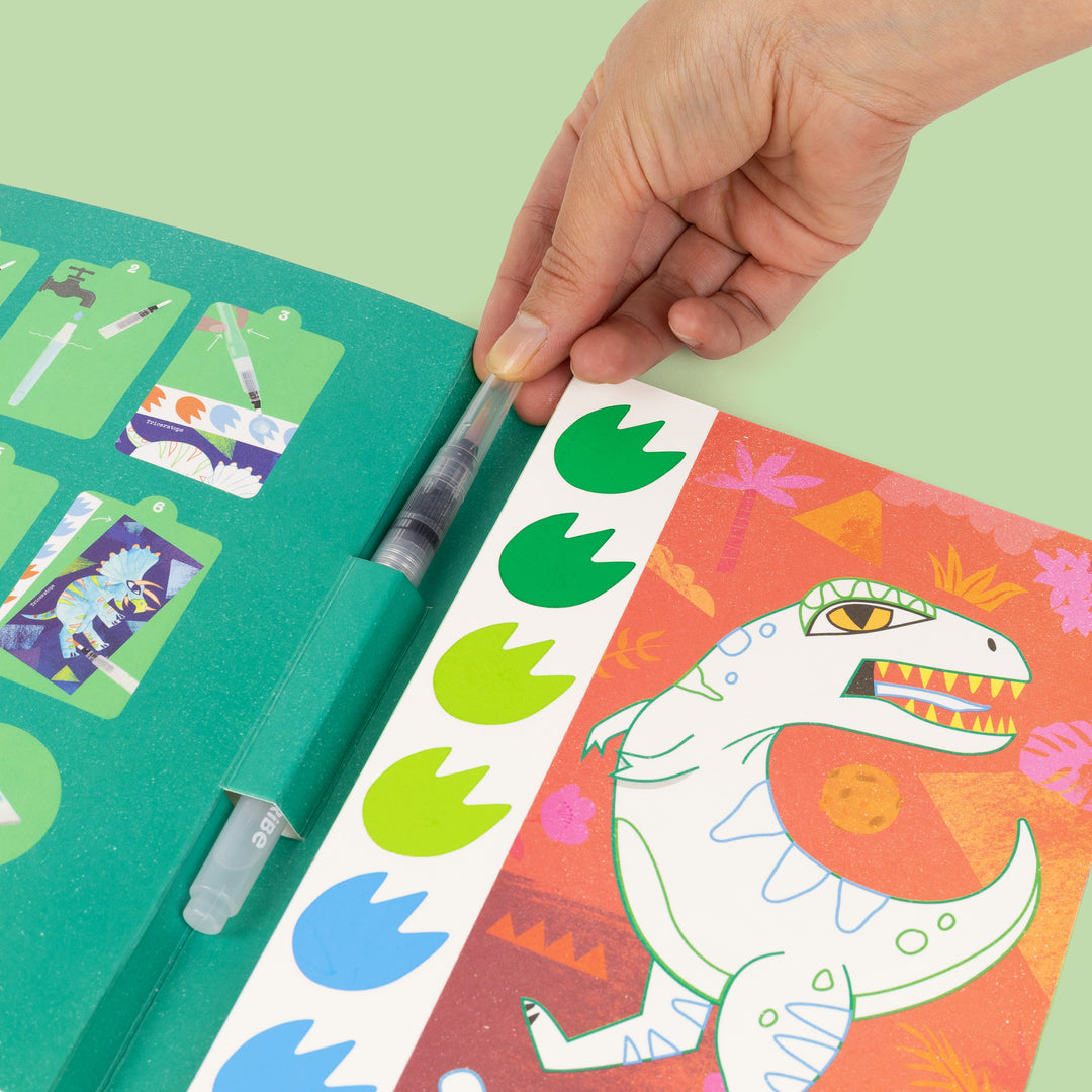 inside of Tiger Tribe Paint a Picture Dinosaurs art kit with watercolor paints, brush, palette, and dinosaur-themed painting scenes. Creative gift for kids. Available at Be Charmed.