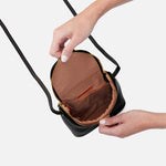 Person opening a black HOBO handbag with brown interior on a white background. Available at Be Charmed