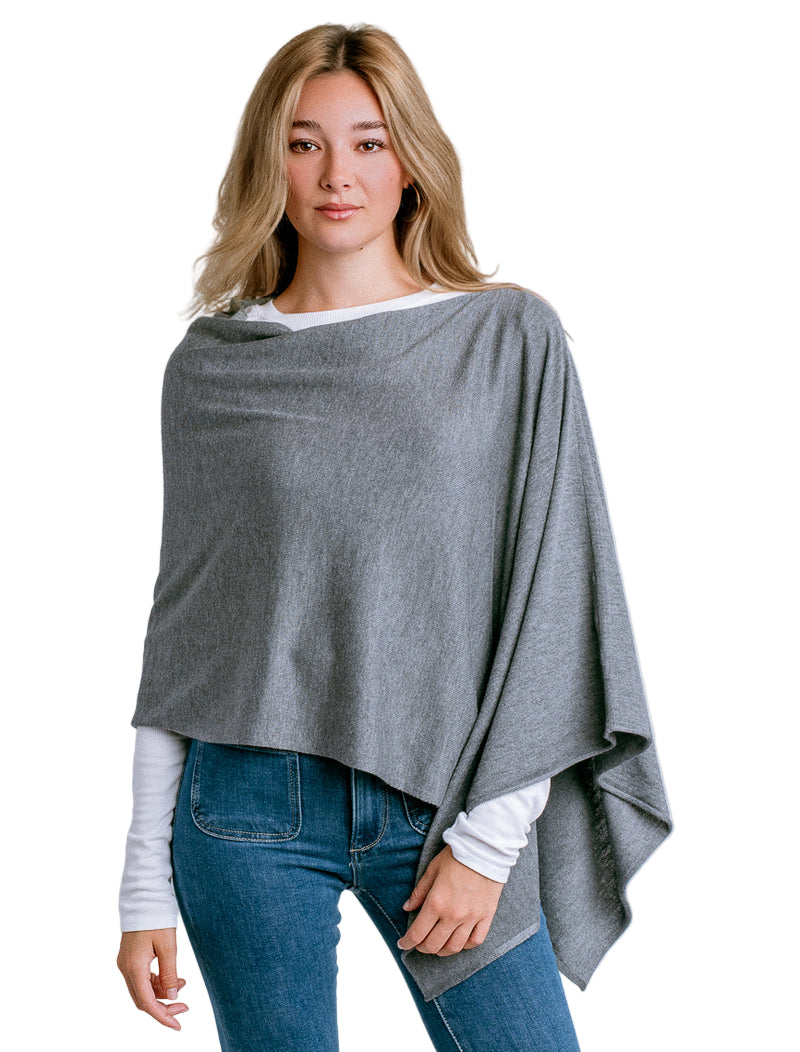 Woman wearing a Kerisma gray poncho over a white shirt and blue jeans on a light white background. Available at Be Charmed