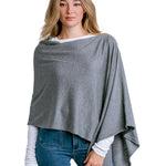 Woman wearing a Kerisma gray poncho over a white shirt and blue jeans on a light white background. Available at Be Charmed
