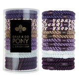 Set of purple and gold hair ties with a cylindrical container labeled 'Grab & Go Pony' on a white background. Available at Be Charmed