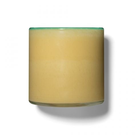 A square-shaped candle with a beige wax layer visible at the top, set against a clear glass base. Available at Be Charmed