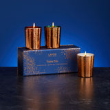 Three copper-colored candles in front of a blue box labeled 'LAFCO' on a dark surface with a blue background.