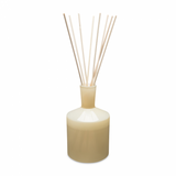 A beige 6 oz reed diffuser with visible reeds and a round base, set against a white background. Available at Be Charmed