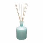 A blue glass reed diffuser with several reeds and a clear lid. Available at Be Charmed