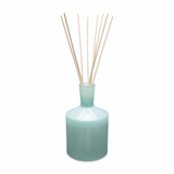 A blue glass reed diffuser with several reeds and a clear lid. Available at Be Charmed