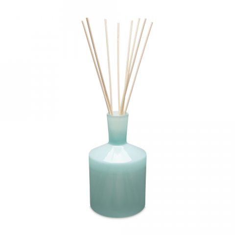 A blue glass reed diffuser with several reeds and a clear lid. Available at Be Charmed
