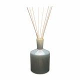 A LAFCO reed diffuser with a grey ceramic bottle and several light wooden reeds inserted, against a white background. Available at Be Charmed