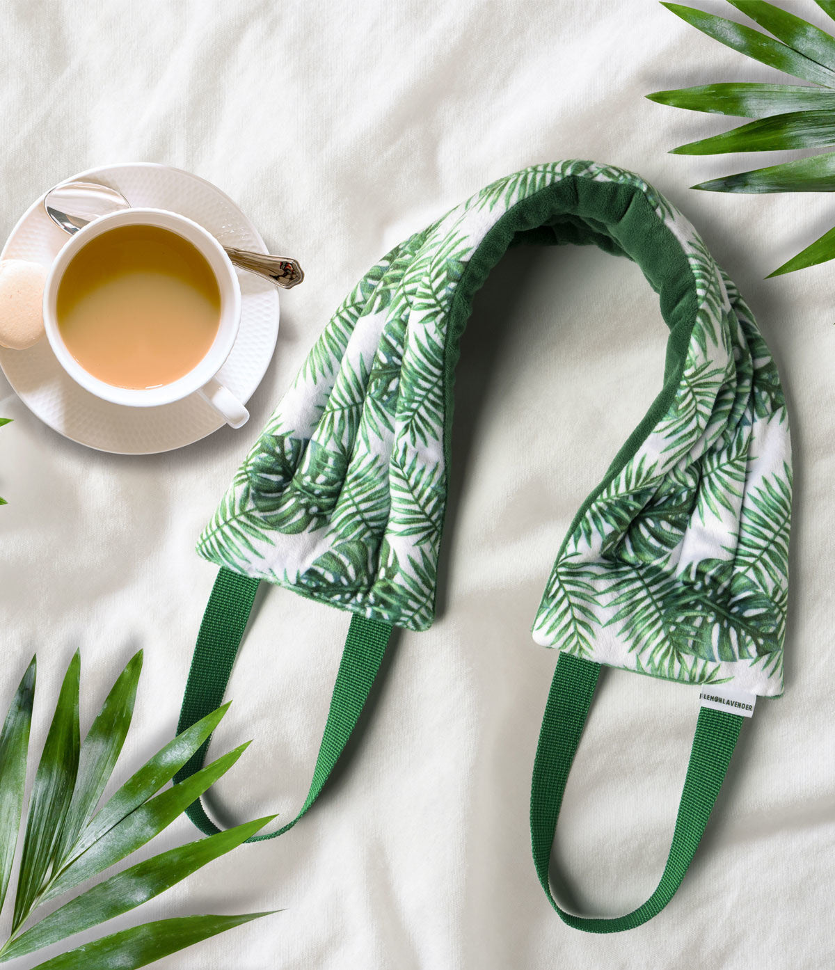 A micfiber neck wrap with a lemon and lavender design, displayed on a flat surface with a cup of tea and green leaves in the background.. Available at Be Charmed