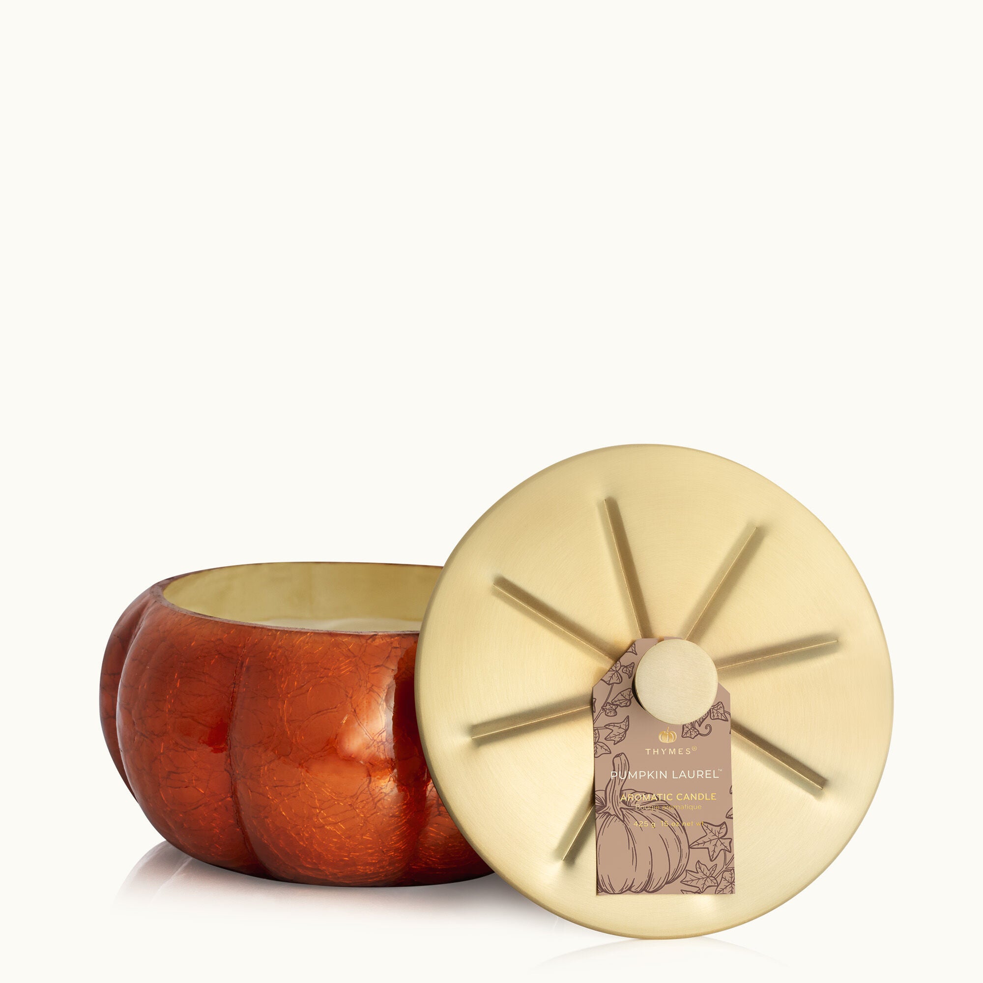 Lid off of Thymes Pumpkin Laurel 15 oz large candle in burnt-orange frosted glass with gold accents—spiced pumpkin scent. Available at Be Charmed.