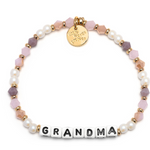 A beaded bracelet with the word 'GRANDMA' written in block letters, featuring peachy love colors and a gold charm. Available at Be Charmed