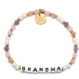 A beaded bracelet with the word 'GRANDMA' written in block letters, featuring peachy love colors and a gold charm. Available at Be Charmed