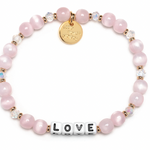Pink beaded bracelet with a gold tag and 'LOVE' charm on a white background. Available at Be Charmed