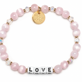 Pink beaded bracelet with a gold tag and 'LOVE' charm on a white background. Available at Be Charmed