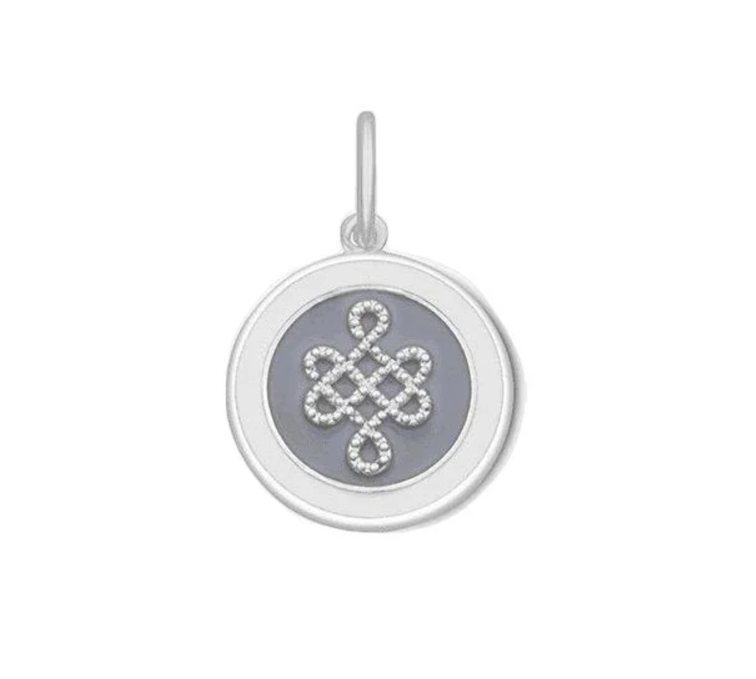 A silver round pendant charm featuring a pale grey Celtic knot or infinity symbol set with small clear stones, mounted on a circular gray inlay, shown against a plain white background. Available at Be Charmed
