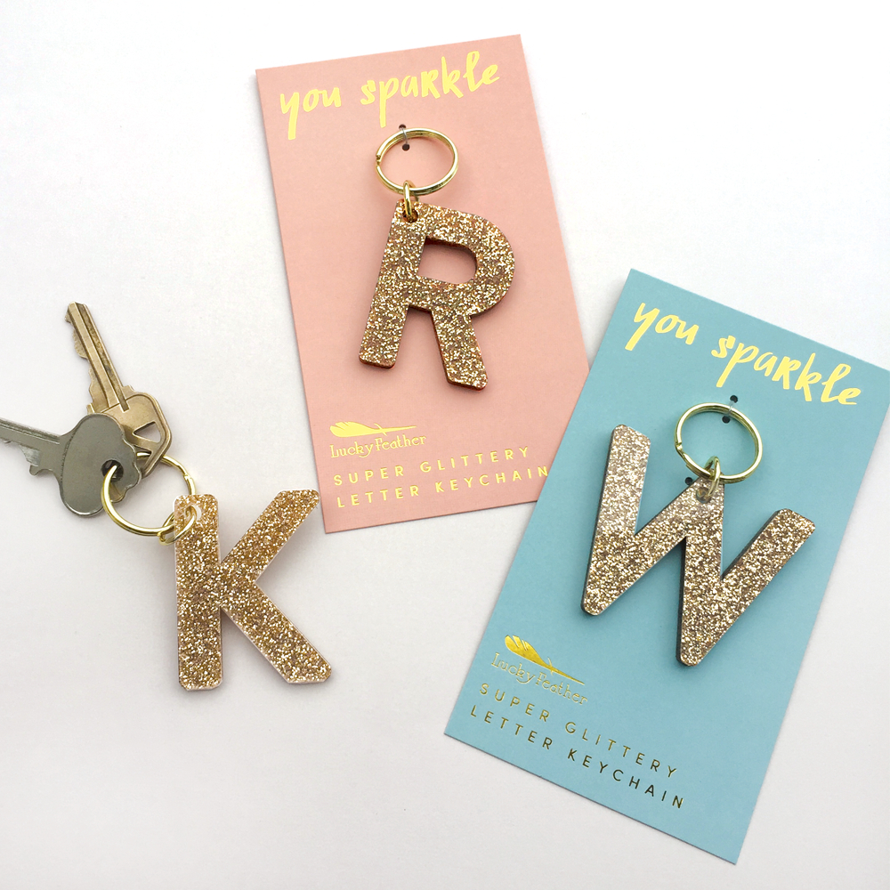 Lucky Feather Initial Keychain featuring glittery acrylic letter charm with gold-tone hardware, personalized for each letter. Available at Be Charmed.