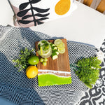 Lime Wooden cutting board with sliced fruits and a glass of lemonade on a patterned blanket.