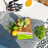 Lime Wooden cutting board with sliced fruits and a glass of lemonade on a patterned blanket.