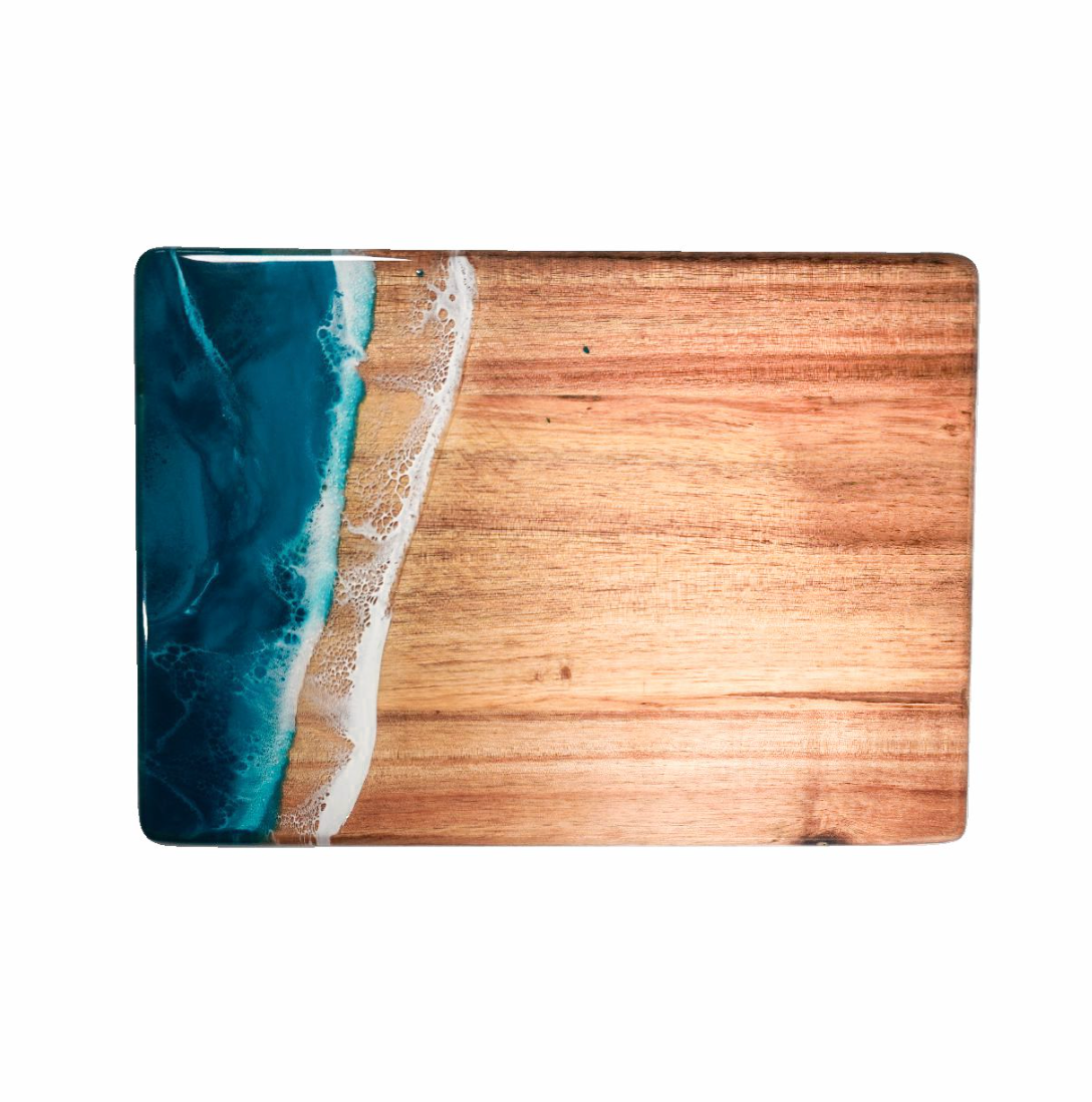 Wooden cutting board with blue resin design on a white background. Available at Be Charmed