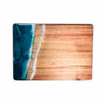 Wooden cutting board with blue resin design on a white background. Available at Be Charmed