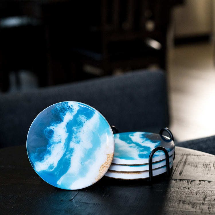 A set of Lynn & Liana round resin coasters with an ocean-like pattern, displayed in a metal holder. Available at Be Charmed