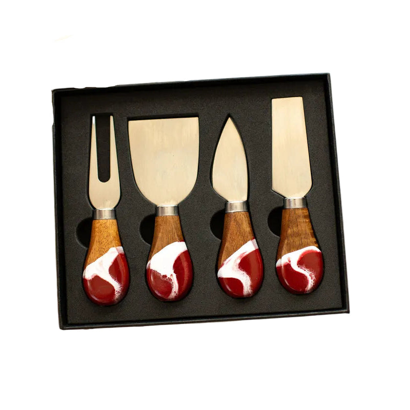 Set of four cheese knives with wooden handles and red and white patterns in a black box held by a person. Available at Be Charmed