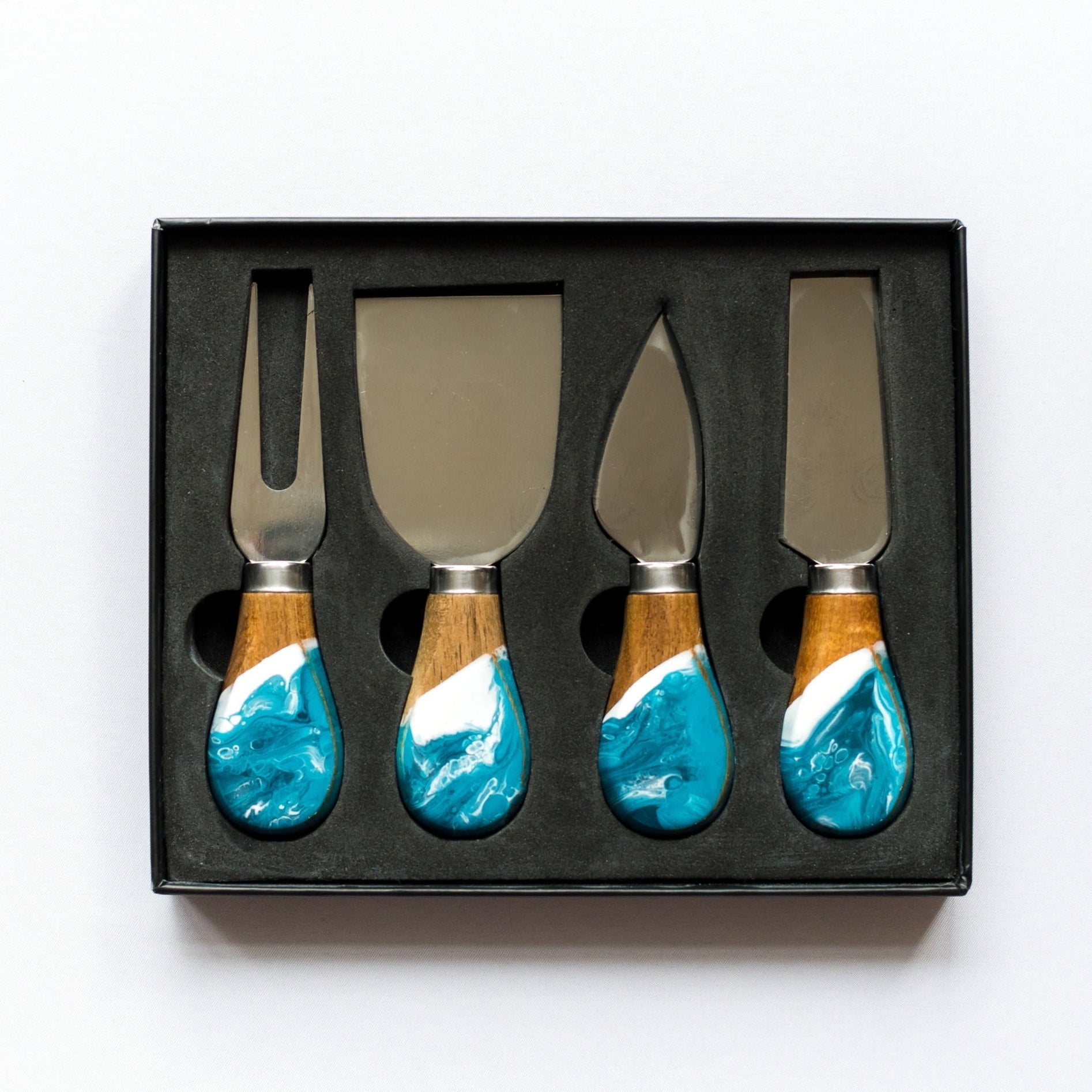 Set of four cheese knives with turquoise and wood handles in a black box on a white background. Available at Be Charmed