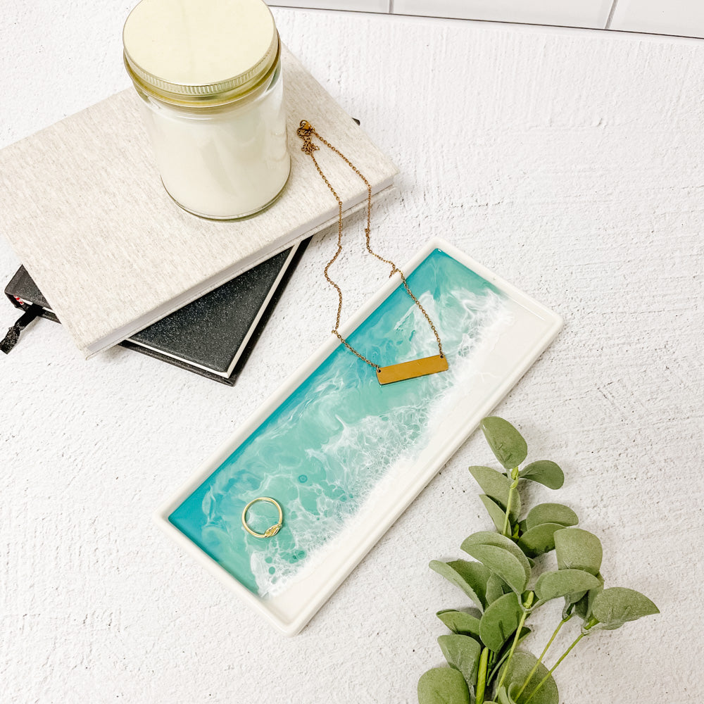 Jewelry set with necklace and ring on a ceramic resin tray next to a candle and notebook on a light surface. Available at Be Charmed