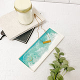 Jewelry set with necklace and ring on a ceramic resin tray next to a candle and notebook on a light surface. Available at Be Charmed